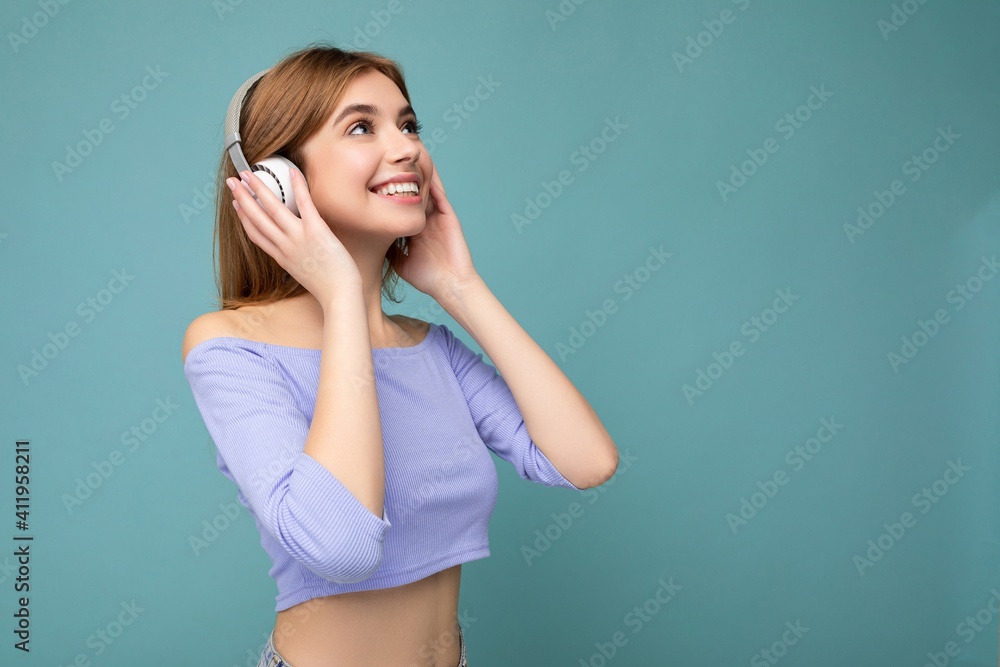 Side-profile photo of beautiful positive smiling young blonde woman wearing blue crop top isolated over blue background wall wearing white wireless bluetooth headphones listening to cool music and Side-profile photo of beautiful positive smiling young blonde woman wearing blue crop top isolated over blue background wall wearing white wireless bluetooth headphones listening to cool music and