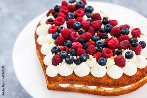 Delicious homemade heart shaped vanilla cake decorated with cream and fresh berries