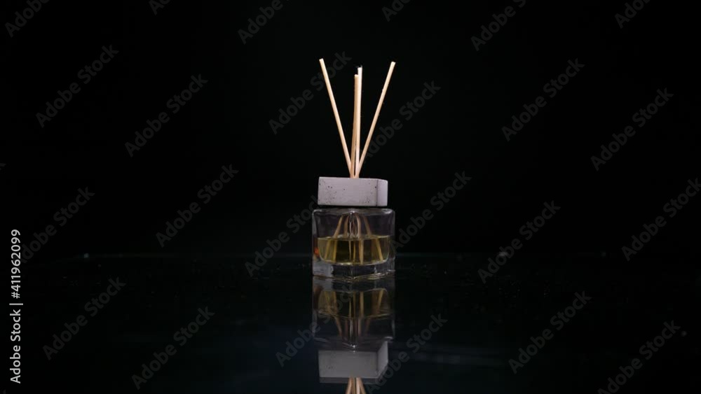 Female hand puts reed diffuser bottle on the mirror surface on black background Female hand puts reed diffuser bottle on the mirror surface on black background