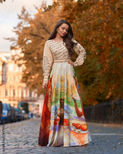 Elegant caucasian woman with long straight brunette hair in bright stylish colorful dress walking city street on a bright day © Dmitry Tsvetkov