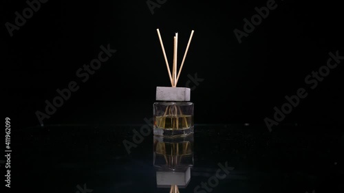 Female hand puts reed diffuser bottle on the mirror surface on black background