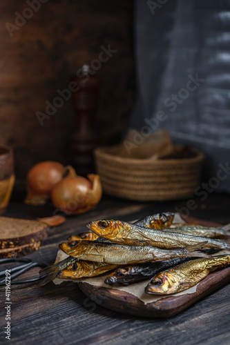 Cold smoked salaka with bread, onion ready to eat. Little golden fish close-up on dark wooden table, healthy natural sea food product, rich of essential Omega-6 fatty acids. Country fisherman style.