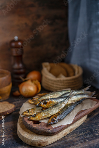 Cold smoked salaka with bread, onion ready to eat. Little golden fish close-up on dark wooden table, healthy natural sea food product, rich of essential Omega-6 fatty acids. Country fisherman style. photo