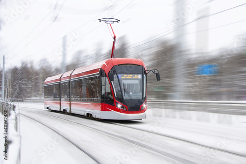 The tram is passing rapidly at a bend in a snow covered city park.