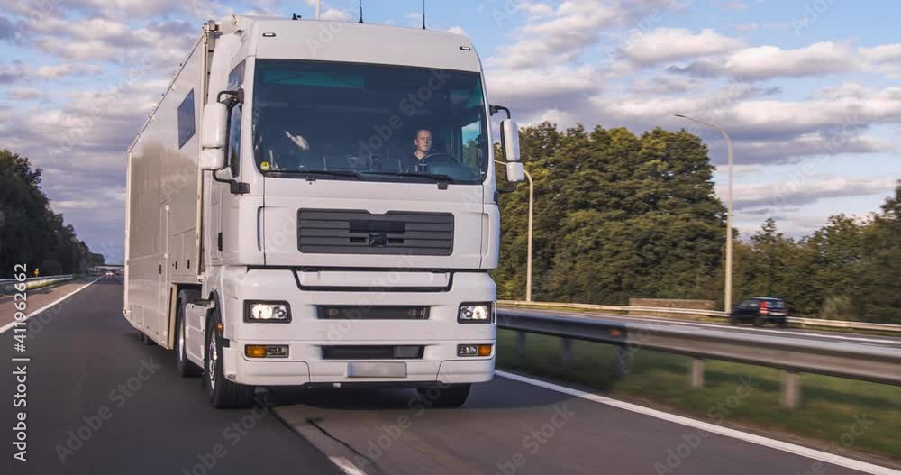 Cargo truck with cargo trailer driving on a highway. White Truck delivers goods in early hours of the Morning - very low angle drive thru close up shot. Cargo truck with cargo trailer driving on a highway. White Truck delivers goods in early hours of the Morning - very low angle drive thru close up shot.