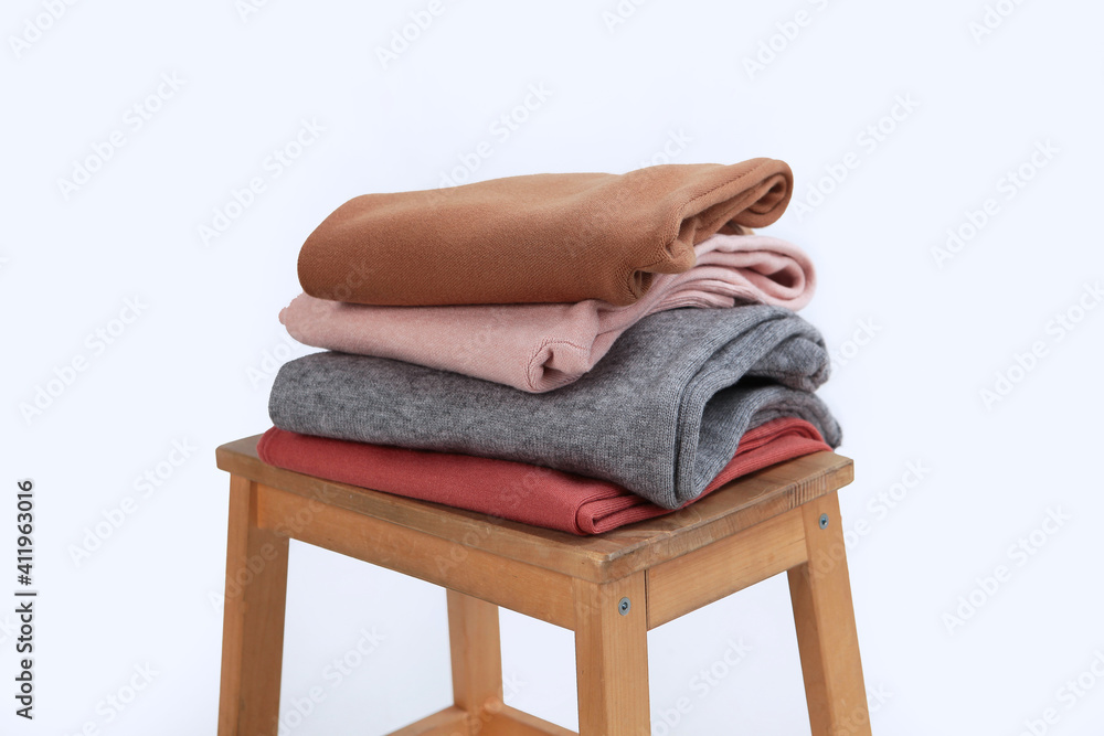 Knitted woolen clothes lie on a wooden chair. Clothes made of natural wool for the cold season. Light background. No people.