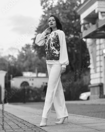 Elegant caicasian woman with long straight brunette hair in white sporty glamour costume and high heels walking city street on autumn day © Dmitry Tsvetkov