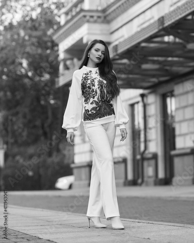 Elegant caicasian woman with long straight brunette hair in white sporty glamour costume and high heels walking city street on autumn day © Dmitry Tsvetkov