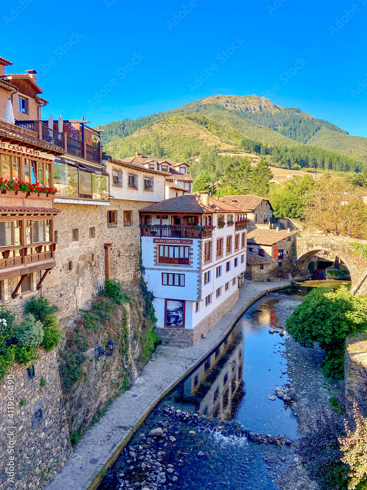 Potes, Spain - September 2, 2020: The medieval arch stone bridge of San Cayetano (Puente de San Cayetano) over the River Quiviesa in Potes surrounded by medieval buildings.