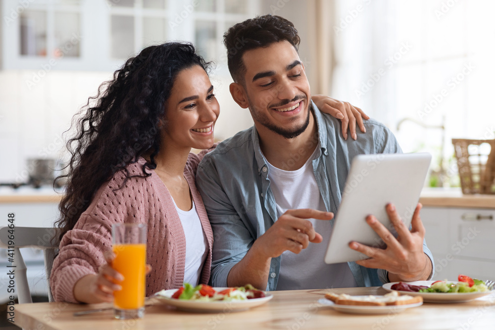 Loving Arab Couple Eating Breakfast Together And Using Digital Tablet In Kitchen Loving Arab Couple Eating Breakfast Together And Using Digital Tablet In Kitchen