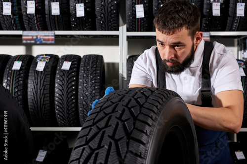 auto mechanic salesman examining tire surface in his shop against the background of tires assortment. automobile, cars, vehicle, transport concept