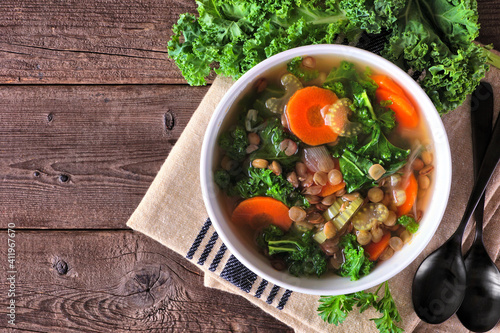 Healthy vegetable soup with kale and lentils. Above view table scene on a dark wood background.