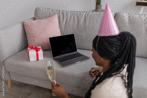 African american woman with champagne and gift box usign laptop photo