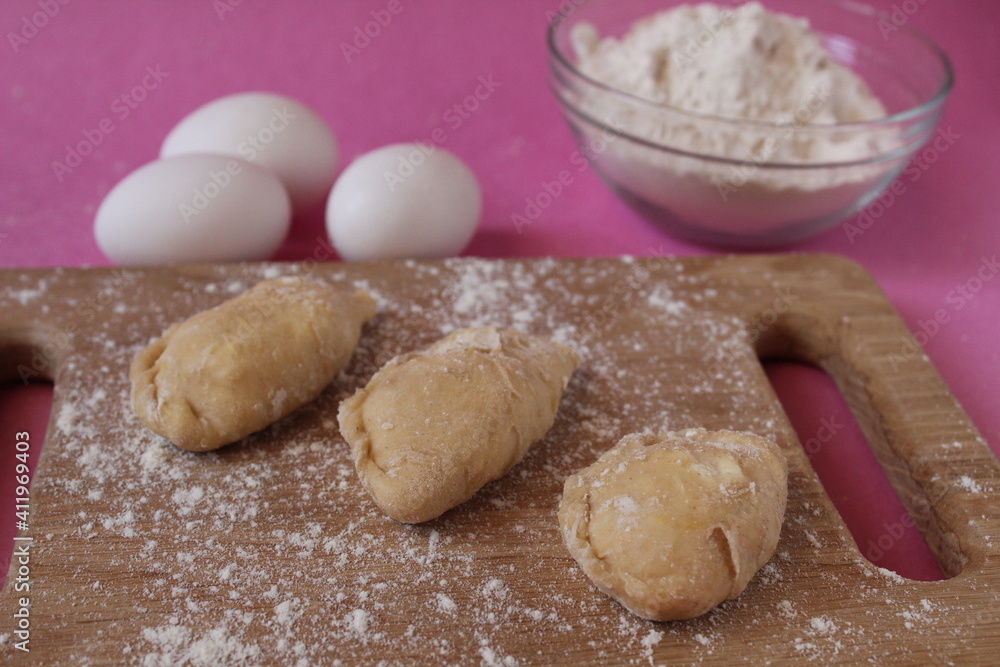 Raw cooking dumplings lie on a board beside egg flour on a pink background view from above Raw cooking dumplings lie on a board beside egg flour on a pink background view from above