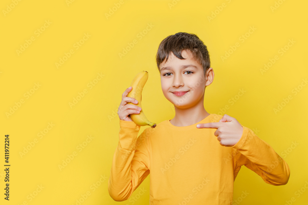 Portrait of a cheerful child boy pretending to be talking on banana like by phone, posing on a yellow background in the studio. Childhood, fruits, emotions, advertising. Close up, copy space  