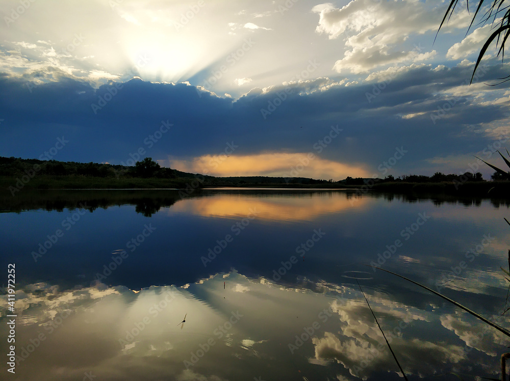 Natural landscape. Sunset over water, reflection of the sun and clouds in the water