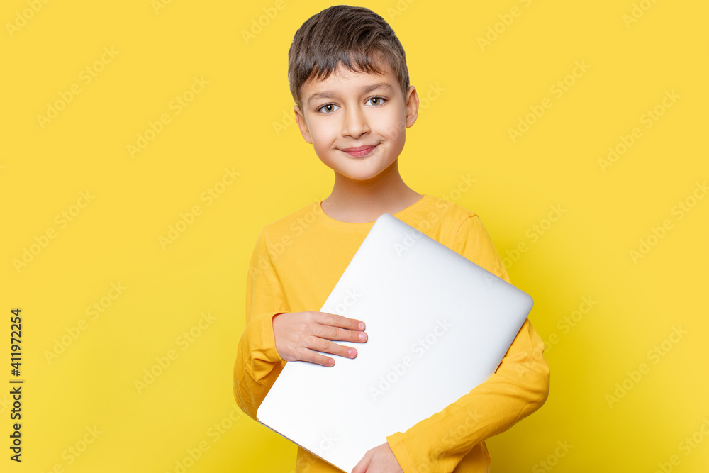 Portrait of focused child boy standing with closed laptop in hands on yellow wall. Portrait of focused child boy standing with closed laptop in hands on yellow wall.