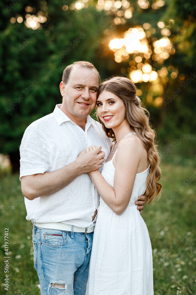 Fototapeta premium Young loving couple hugging on the green grass in the park. Beautiful woman and man gently touch each other. Beautiful couple in love. girl in the dress and the guy in the shirt. valentines day