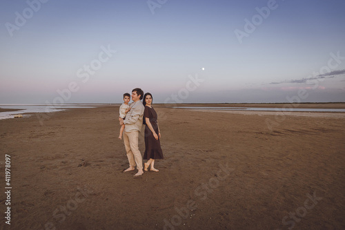 Beautiful young family on the evening beach. Family look of natural linen clothing. Copy space.