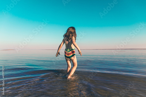 A cute little girl in a knitted swimsuit enters the cold sea water for the first time in the season. Copy space. Toned minimalism photo.