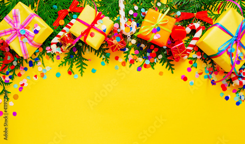 pine branches and colorful gift boxes on a yellow background top view. Space for the text.