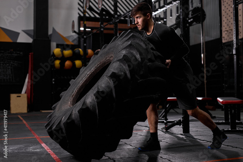 spotsman pushing drawn tire to build strength at modern fitness center. Male in sportswear is engaged in cross fit and workout. Sport, healthy lifestyle, bodybuilding, crossfit, workout concept