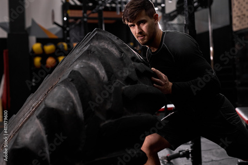Confident male athlete doing tire-flip exercise indoors in modern gym. Cross fit and workout. Strong and handsome athlete in sportswear. sport, healthy lifestyle