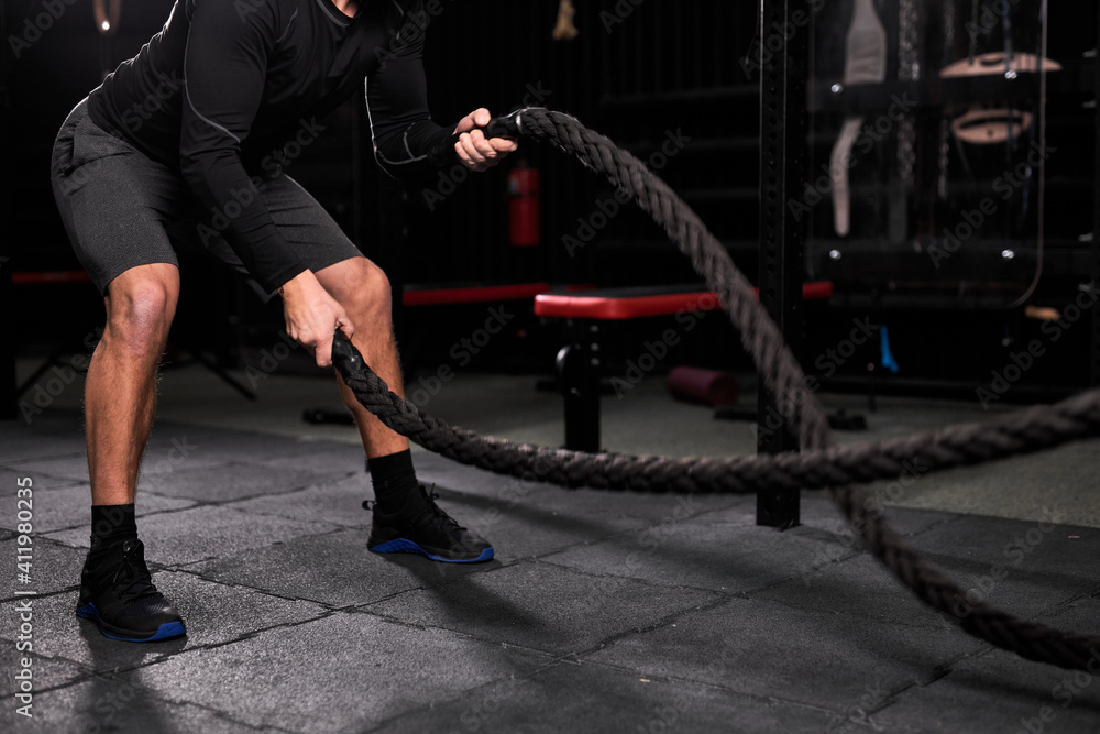 Naklejka premium Cropped athletic man doing cross fit exercises with rope at gym, concentrated and focused on training, workout. people and sport, cross fit concept