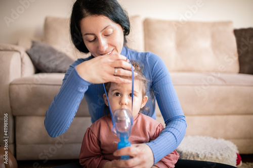 Mother helps her little girl to makes inhalation at home.During coronavirus COVID-19 photo