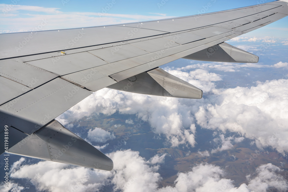 View from passenger window of commercial airplane, clouds on blue sky visible under aircraft wing View from passenger window of commercial airplane, clouds on blue sky visible under aircraft wing