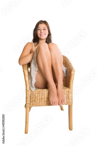 Laughing young woman sitting on a wicker chair in front of white studio background 