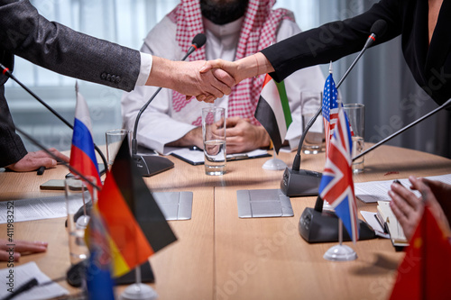 contemporary intercultural delegates shaking hands after successful meeting press conference with microphones  in boardroom office. executives signed a bilateral agreement