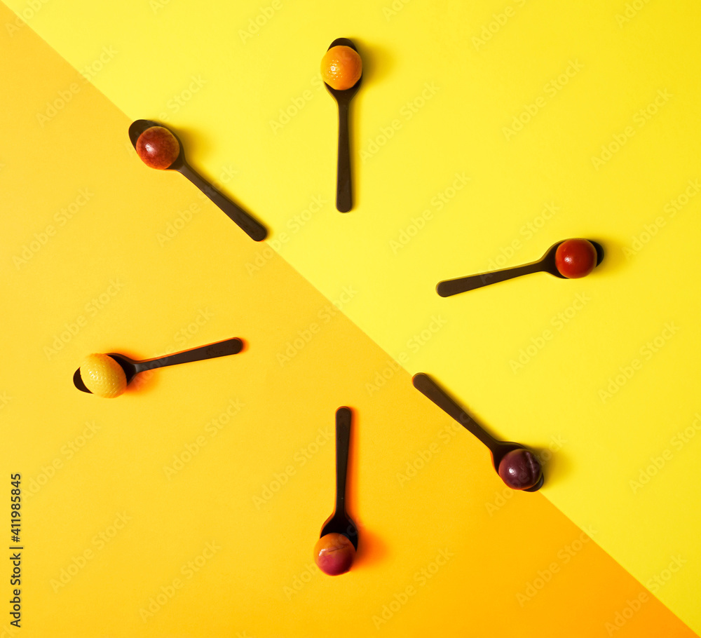 Arrangement of six chocolate spoons with marzipan fruit shaped candies in different colors and shapes - lemon, plum, orange, apple against diagonal of yellow and orange background. Taken from above. Arrangement of six chocolate spoons with marzipan fruit shaped candies in different colors and shapes - lemon, plum, orange, apple against diagonal of yellow and orange background. Taken from above.