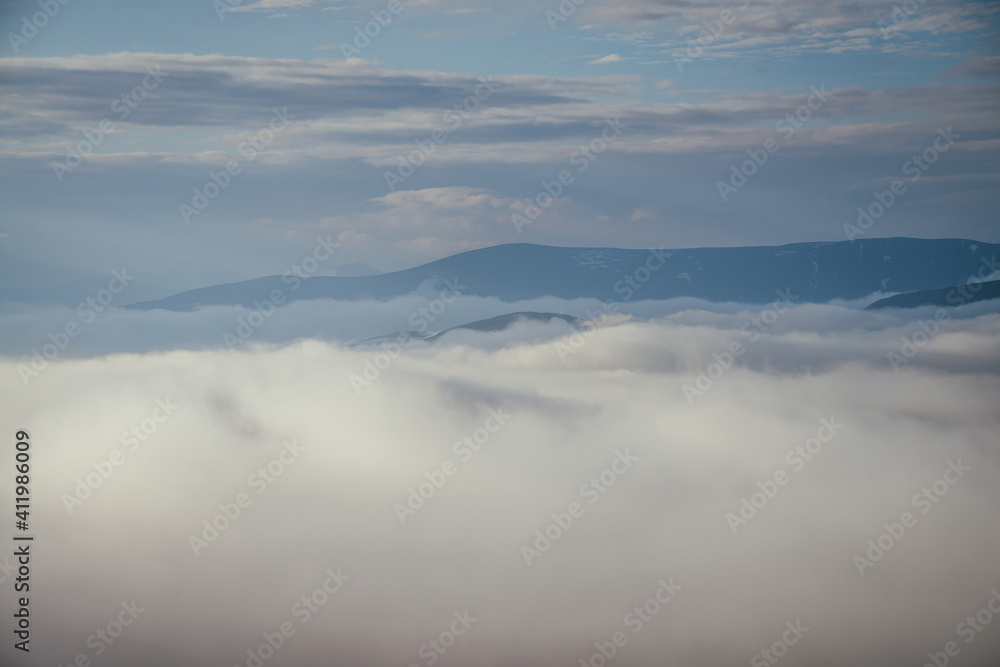 Awesome alpine landscape with snowy mountain range on horizon above clouds. Atmospheric minimal alpine scenery with big mountain ridge above many low clouds. Cloudy sea, cloudy ocean in mountains. Awesome alpine landscape with snowy mountain range on horizon above clouds. Atmospheric minimal alpine scenery with big mountain ridge above many low clouds. Cloudy sea, cloudy ocean in mountains.