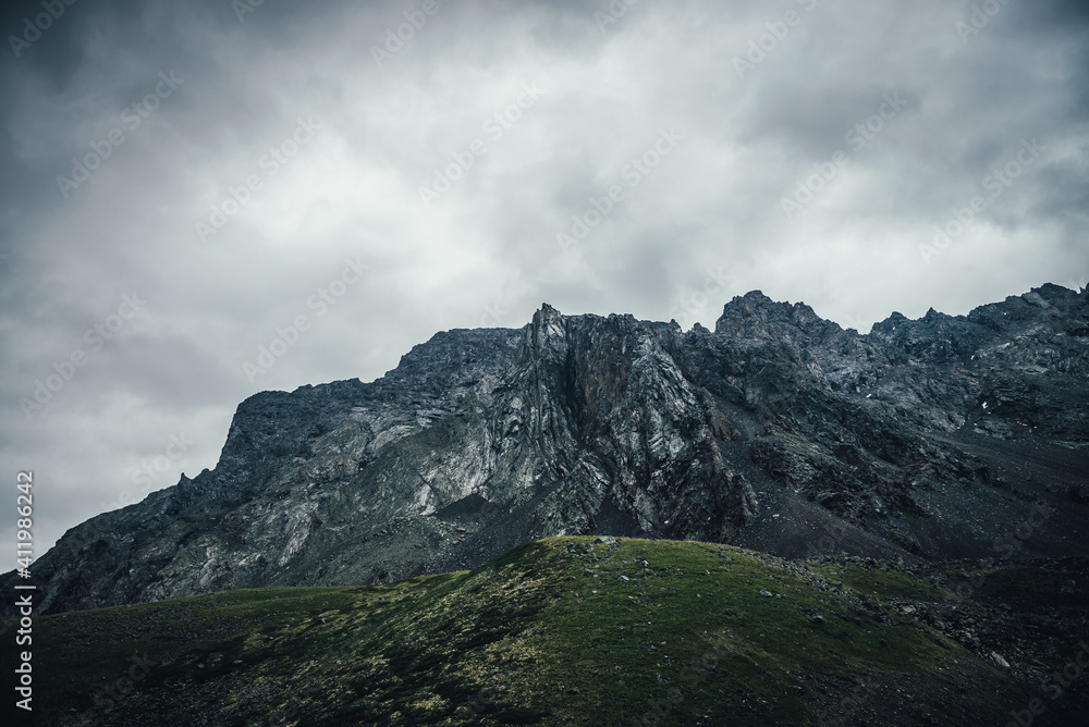 Dark atmospheric landscape with rocky mountain wall under gray cloudy sky. Rocky pinnacle in lead gray cloudy sky. Dark mountain peak in overcast weather. Gloomy minimalist scenery with high mountains Dark atmospheric landscape with rocky mountain wall under gray cloudy sky. Rocky pinnacle in lead gray cloudy sky. Dark mountain peak in overcast weather. Gloomy minimalist scenery with high mountains