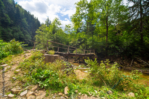 The old wooden weak bridge over small river in mountain forest