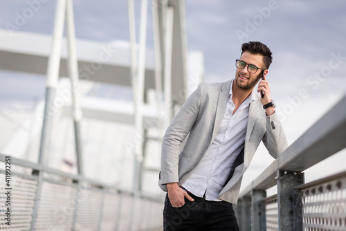Happy young businessperson on bridge talking on smartphone. Yuppie outdoors talking on mobile and smiling
