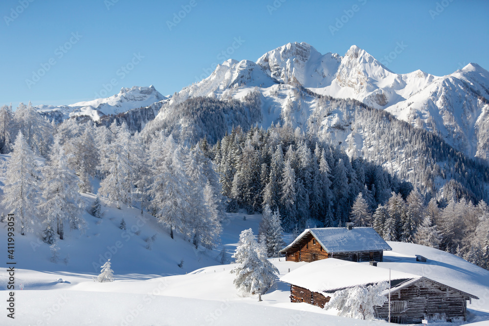 Beautiful winter mountain landscape with snowy forest and traditional alpine chalet. Sunny frosty weather with clear blue sky
