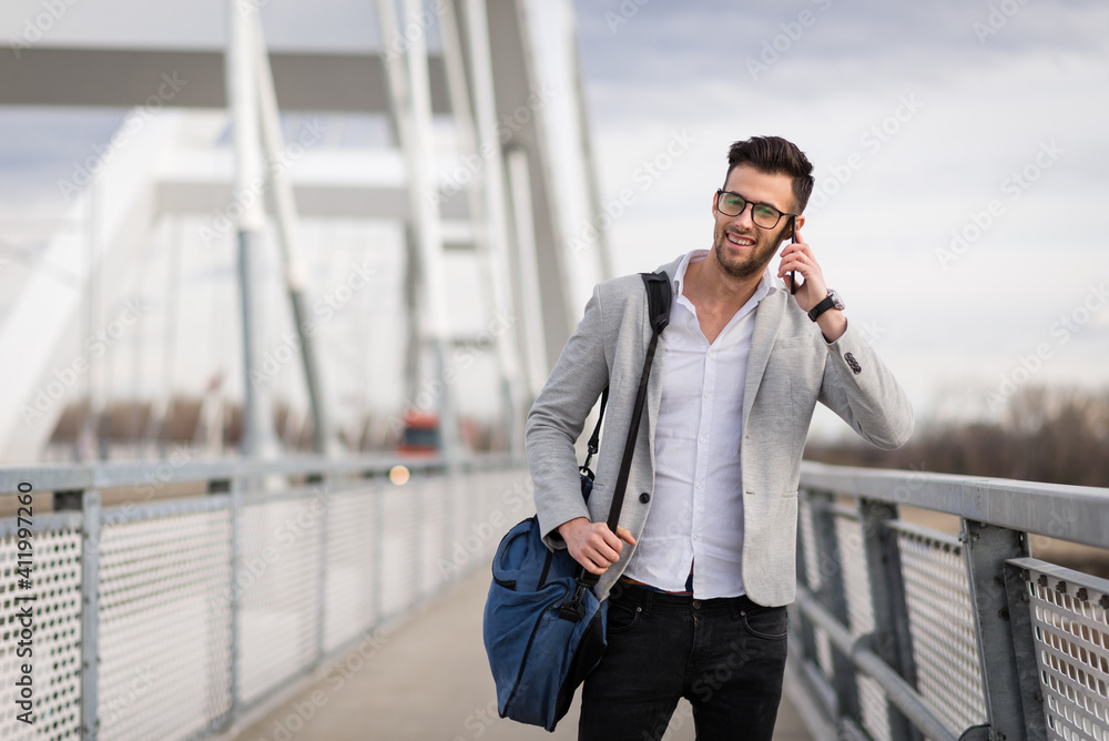Yuppie outdoors talking on smartphone and smiling. Happy young businessperson on the bridge holding bag Yuppie outdoors talking on smartphone and smiling. Happy young businessperson on the bridge holding bag