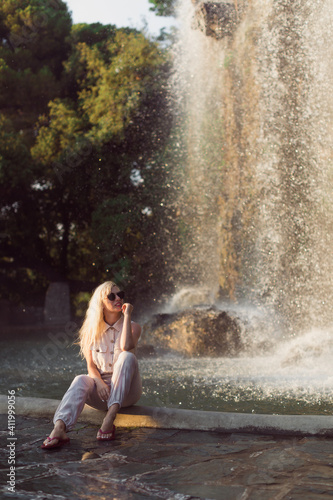 Fototapeta Naklejka Na Ścianę i Meble -  The beautiful young woman is sitting on the waterfall background