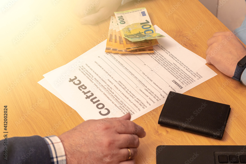 Obraz premium selective focus of a contract and money put on the table ready to make a deal or extortion on a wooden table with a laptop and a mobile phone