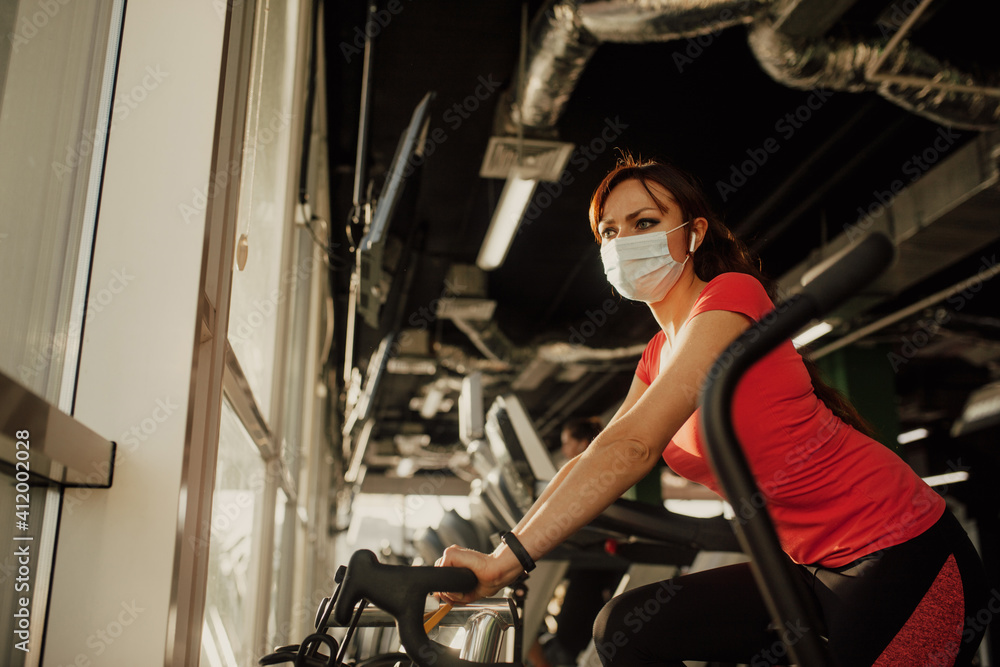 Obraz premium An active woman in a protective medical mask training in gym, during COVID-19 epidemic. Sport and quarantine.