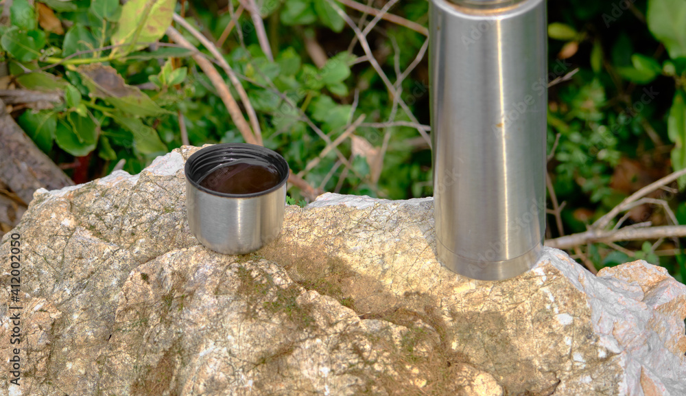 Caffe mug and heat sealing thermos cover made of stainless steel on thee rock by taking photo during trekking in wild nature in forest Caffe mug and heat sealing thermos cover made of stainless steel on thee rock by taking photo during trekking in wild nature in forest