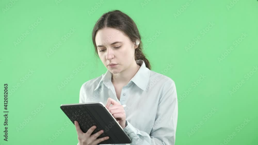 A young business girl leads an online conference in headphones with a digital tablet in her hands on a green isolated background. Online work. Remote work during a pandemic. Stay at home.