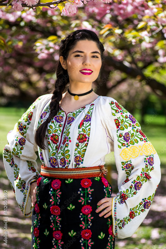 Beautiful young woman posing in romanian traditional costume in the park