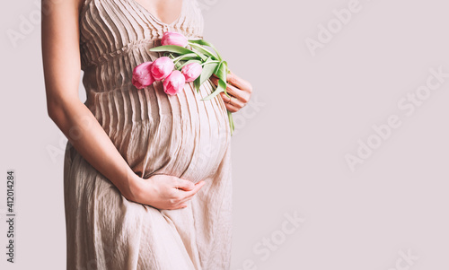 Photo Beautiful pregnant woman with tulips flowers holds hands on belly