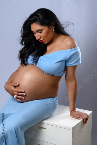 BEAUTIFUL PREGNANT WOMAN WITH SHOES ON THE BELLY IN A BLUE DRESS
