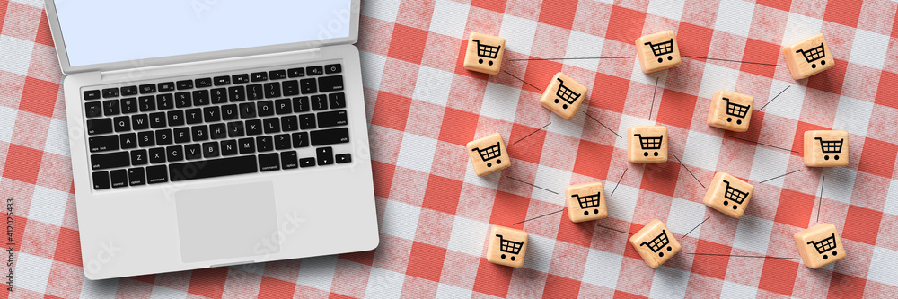 cubes with shopping cart symbols that are connected with laptop on kitchen table background