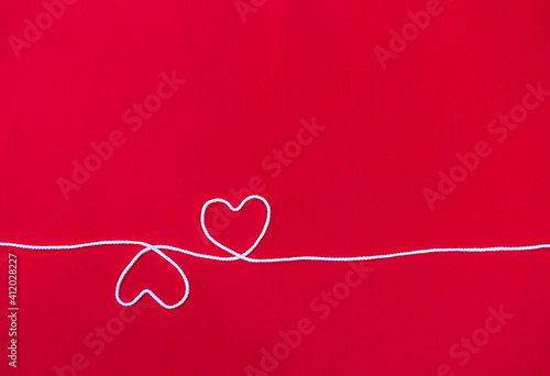Two white cotton thread in heart shape on red fabric background, valentine card background idea, love and romance concept