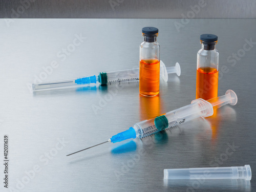 Selective focus. Syringe for injection and ampoules with orange coronavirus vaccine on a silver aluminum background. Covid-19 pandemic medical concept. Flat lay.